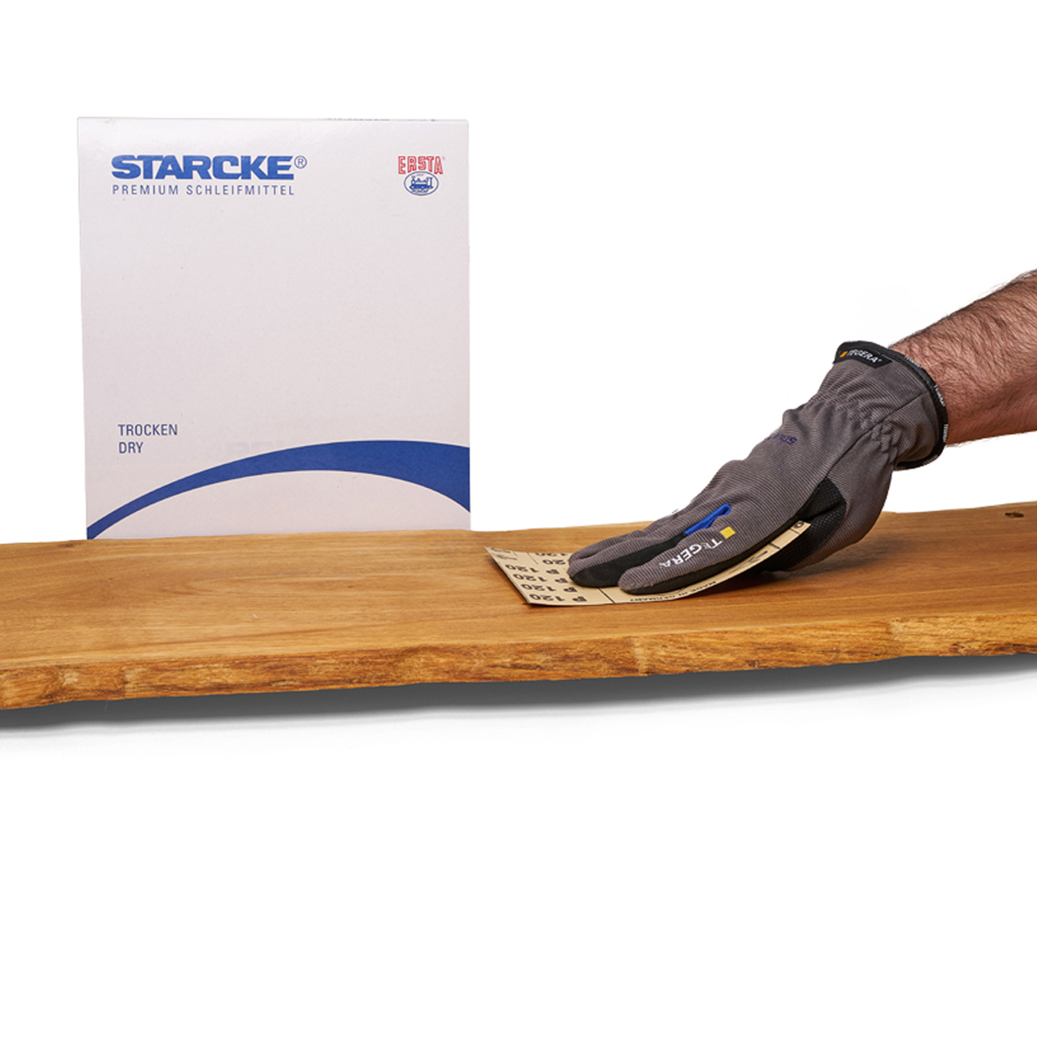 Schleifpapierkarton im Hintergrund und davor schleift eine Hand das Holz.