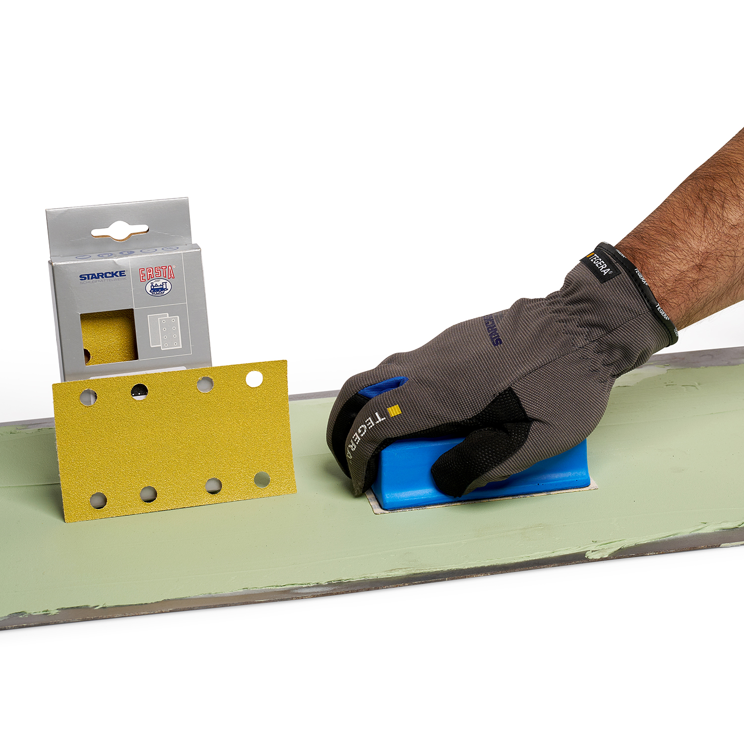Hand schleift Oberfläche ab. Im Hintergrund ist ein Schleifstreifen mit Karton.
